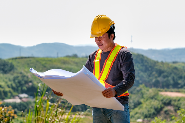 Engineer hold the construction paper plan and look to it in front of mountain view.
